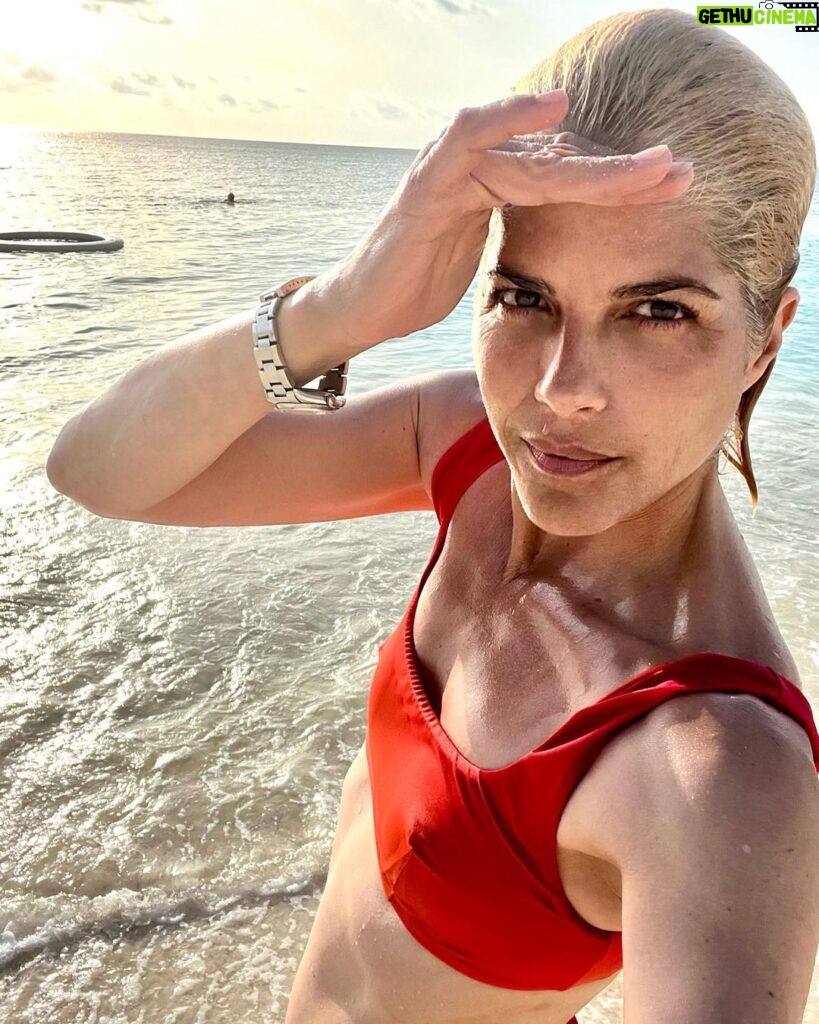 Selma Blair Instagram - It is a gift 🌊 Image description: Selma is standing on the beach with the sun and ocean behind her. She is wearing on orange bikini top and looking at the camera.
