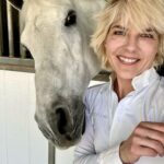 Selma Blair Instagram - This is my social life and it’s pretty grand. Mr Nibbles gives me all the emotions. 🎭 It’s getting hot out here, drink your water 💁🏼💦 Image Descriptions: Image 1: Selma has short blonde hair and wears a white long sleeve shirt. She is smiling and standing next to her white horse. Image 2: Selma wears a white long sleeve, tan pants, boots, and a helmet and is sitting outside. Video: Video of Selma riding her horse Image 3: Selma poses with her horse Image 4: Close up image of Selma in her riding gear. Image 5: Selma poses with her horse.