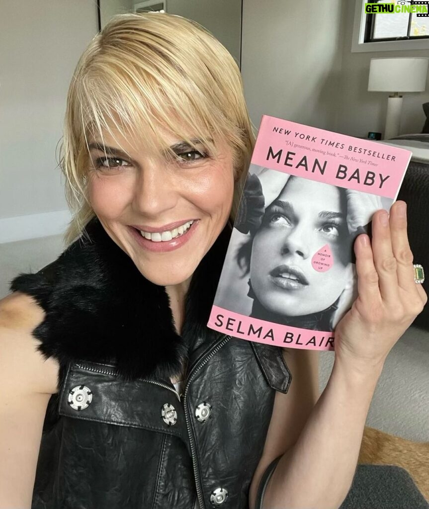 Selma Blair Instagram - Mean Baby is pretty in pink and paperback. 💞 Available tomorrow, May 9th. Image description: Selma has short blonde hair and wears a black top. Selma holds a paperback copy of her book, Mean Baby.