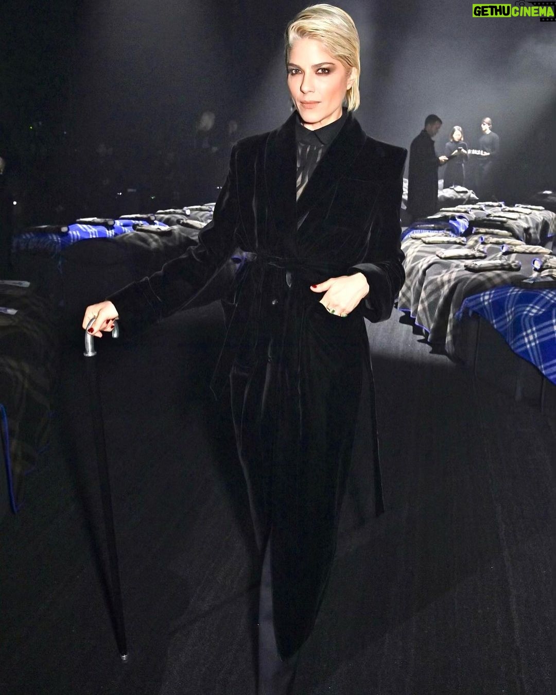 Selma Blair Instagram - The evening of Burberry. 🗡️ Image Descriptions: Image one: Selma has short blonde hair and wears a long black velvet coat. She is standing on the runway at the Burberry show with her cane with one hand in her pocket. Image two: Selma stands in front of orange wall. Image three: Selma sits with Edward and Naomi. Edward is wearing all black and Naomi is wearing a grey suit. Image four: Selma and Georgia are standing and both wearing black. Image five: Selma is standing in profile wearing a white robe while getting her hair done. Image six: Selma leans against an orange wall and is looking to the left.