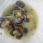 Stanley Tucci Instagram - Serves 4 (in my house) 1kg clams Half an onion diced One garlic clove split in two Two pepperoncini 1 cup of white wine 1 sprig of thyme 2 sprigs of parsley Handful chopped parsley Evoo Clean the clams by submerging in cold very salty water (this purges them of grit!) Discard any open ones. Sauté the onion and garlic in a pan in evoo Add one or two pepperonci 🌶 Add the white wine, raise heat to high to burn off alcohol Add the clams and a sprig of thyme, two sprigs of parsley 🌿 Season with salt and pepper Place a top over the pan and the clams will start to open. After two minutes remove the cover and shake the pan gently. If the clams have not started to open place lid back on for a minute Make sure all (or nearly all) the clams have opened. Discard those that have not. Lower heat to a simmer and add chopped parsley and a slug of EVOO Serve with toasted bread (and in my case a tomato salad). This is my wife’s favorite. (One of, she’s a glutton).