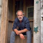 Steven Ogg Instagram – Squeezing it out
during a lunch break on location.
Pinching off
some poetry read.
One take. One attempt. 
Many chipmunks.

“He loved her and she loved him.
His kisses sucked out her whole past and future or tried to
He had no other appetite
She bit him she gnawed him she sucked
She wanted him complete inside her
Safe and sure forever and ever
Their little cries fluttered into the curtains

Her eyes wanted nothing to get away
Her looks nailed down his hands his wrists his elbows
He gripped her hard so that life
Should not drag her from that moment
He wanted all future to cease
He wanted to topple with his arms round her
…
In their entwined sleep they exchanged arms and legs
In their dreams their brains took each other hostage
In the morning they wore each other’s face” (I incorrectly said faces….it happens…apologies!)

🎶Music to accompany- @danmanganmusic new single “YOU KNOW IT.”🎶
#poetry #outhouse #DropOneOff #tedhughes Outhouse
