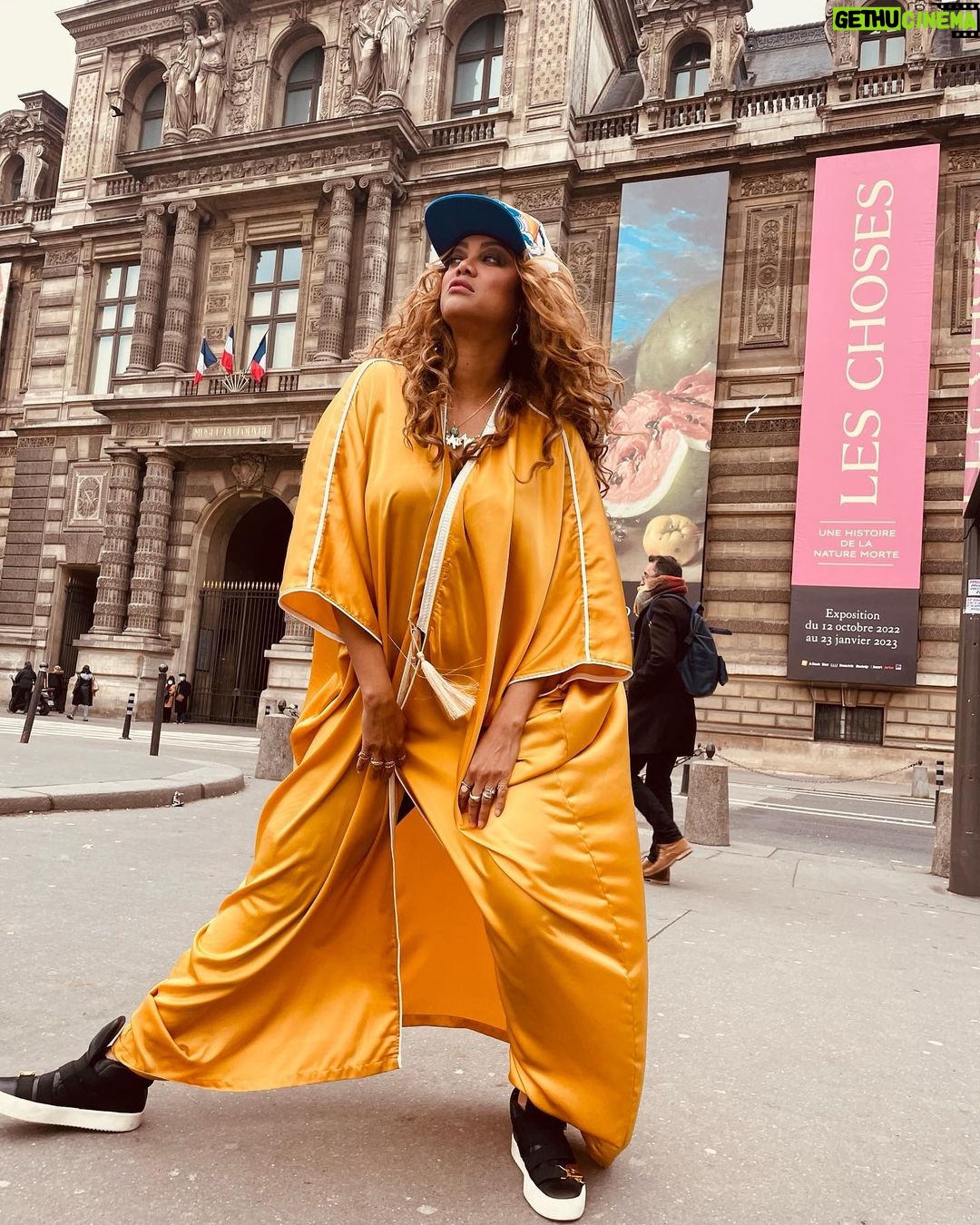 Tyra Banks Instagram - As a teenager, I walked the streets of Paris, going from casting to casting, hoping to get chosen. Cut to decades later… Moments after the @louisvuitton x @kidsuper men’s fashion show, and I have no shame in getting my pose on in front of the @museelouvre rocking a Louis cap Colm gave me and a golden kaftan I picked up from an Abu Dhabi desert hotel gift shop. Every #Paris street is a photo studio. Remember that. 💪🏽🇫🇷📸