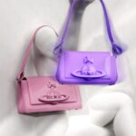 Vivienne Westwood Instagram – This season’s Hazel bag features bondage-inspired elements, reminiscent of our ‘Erotic Zones’ collection from Spring-Summer 1995. The pink patent finish of the Hazel is synonymous with the pink latex signage from our iconic SEX boutique, currently known as Worlds’ End. The style is also available in a Purple colourway this season, offered in both small and medium sizes.⁠
⁠
Now available online and across our boutiques. ⁠
⁠
#VWSS24