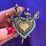 Dita Von Teese Instagram - The Valiant Heart Brooch To know love is to know its sweeps of passion and pain, and of the self-knowledge and resilience each one of us can find strength in, as robust as a well-crafted sword. Four swords brace the heart, the universal symbol of love and joy, in this hand-sculpted #brooch, finished in bronze and based on a vintage #1940s era treasure from my collection. It is a favorite because of its romantically regal effect, evoking #heraldic insignia. Take heart, valiant ones! This is a badge not about the end, but rebirth. A meaningful gift—yes, even for yourself. Swarovski crystal elements accent the swords and heart outline in diamanté and garnet, as well as turquoise beads. The center heart is suitable for engraving initials or a message. Made in the USA 🇺🇸 Exclusively at luxfaire.com