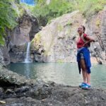 Laura Felpin Instagram - J’étais partie à l’ile Maurice après LA grande rupture.Je venais de regarder Mange Prie Aime, et je n’étais pas indifférente à l’idée de trouver Javier Bardem en bord de mer. Quand je suis arrivée à l’hôtel, j’ai compris que c’était un endroit spécialisé dans les lunes de miel. Interdit aux enfants. Que des adultes consentant de se bouffer la gueule H24 dans une ancienne demeure d’époque datant de la colonisation. Zéro respect pour les anciens esclaves, et pour moi donc. Je l’ai pris très personnellement. Sur mon lit, il y avait deux serviettes en forme de cygnes qui formaient un coeur des pétales de roses, un grand classique de l’hôtellerie de blanc. C’est là bas que j’ai purgé. Mais après mon sixième enveloppement au rhassoul plus finition gommage quand il n’y avait définitivement plus rien a gratter de moi, j’ai décidé de sortir de ma zone de confort, en réservant une randonnée: les 7 cascades. J’allais rencontrer des gens et on se parlerait sur WhatsApp pour se revoir à Port Louis. Parce que maintenant ma vie était ici. Je porterais du lin et je pratiquerais le tantrisme. Mais quand je suis arrivée, j’étais la seule a avoir réservé et la seule chose que le guide m’a dit c’est : vous n’êtes pas bien habillée pour l’activité, puis il m’a demandé de ne pas parler pour respecter la forêt. Pendant 4heures. Ceux qui me connaissent savent.Il aurait pu me demander de mettre mes doigts dans un toaster, mais 4h sans parler. Alors j’ai pensé. J’ai pensé qu’il faudrait trouver un signe, entre ex, comme les motards quand ils se croisent, pour se dire qu’on se re-connait, même 10 ans après. Un truc pour dire : je te sais. Et puis j’ai croisé un groupe de françaises. Pour elles, j’étais Annick en randonnée, y’avait pas plus cliché. On a fait des photos. Le guide m’a ensuite demandé de poser devant tous les points clefs de la randonné, sur le site ça lui ferait de la pub. Il m’a demandé de lever les bras, et d’avoir l’air je cite « mieux heureuse ». J’ai pleuré, on a continué à marcher. Si vous êtes dans votre grande rupture : je vous fait cadeau de ces photos, ça m’a mis longtemps mais aujourd’hui ce sont mes préférées. C’est vrai que j’étais mal habillée.