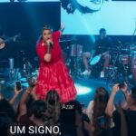 Maria Rita Instagram – Em cada passo, a dança audaciosa na corda bamba da vida. Aquarianos, como equilibristas, acreditam que, mesmo nas dores, a esperança é a força que os impulsiona.

Lutando por um mundo mais justo, eles sabem que o show de todo artista, e de cada coração rebelde, precisa continuar.

#EMR

#PraTodosVerem Maria Rita cantando em cima do palco vestida de vermelho com a banda atrás. No telão atrás dela, um desenho de Mariele Franco.