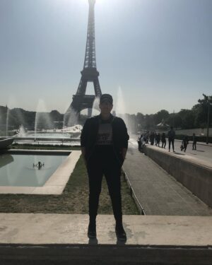 Sara Ramirez Instagram - That time I traveled with a good platonic friend 🎉 @thefreeactorvist 🎉who just got it (and still gets it) and there was mutual support and ease in co-creating a fucking GREAT time! Celebrating good platonic friendships because they matter too! 
📷🎥: @thefreeactorvist 
.
.
.
Image 1: Sara reclaiming Paris for themselves. They are facing the camera, sunglasses on, hands in pockets, standing in all black joggers, boots, jacket, black tshirt that reads “binaries are for computers” in black font over a square of white zeros and ones, ballcap that has “X=“ in white. Paris and the Eiffel Tower in the background, sunny clear sky. 

Image 2: Same everything except Sara’s head is turned to camera right.

Video: Sara singing “You Oughta Know” by Alanis Morissette into a green lit mic at a red light district karaoke bar. Sara is wearing white joggers, a camo sweatshirt and same black ballcap with the “X=“ in white. Sara is FEELING IT. The bar is low lit in reds, purples, yellow and green, passersby in the background by the front door -some walking by and one just chilling watching from the cobblestone walkway outside.