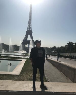 Sara Ramirez Instagram - That time I traveled with a good platonic friend 🎉 @thefreeactorvist 🎉who just got it (and still gets it) and there was mutual support and ease in co-creating a fucking GREAT time! Celebrating good platonic friendships because they matter too! 
📷🎥: @thefreeactorvist 
.
.
.
Image 1: Sara reclaiming Paris for themselves. They are facing the camera, sunglasses on, hands in pockets, standing in all black joggers, boots, jacket, black tshirt that reads “binaries are for computers” in black font over a square of white zeros and ones, ballcap that has “X=“ in white. Paris and the Eiffel Tower in the background, sunny clear sky. 

Image 2: Same everything except Sara’s head is turned to camera right.

Video: Sara singing “You Oughta Know” by Alanis Morissette into a green lit mic at a red light district karaoke bar. Sara is wearing white joggers, a camo sweatshirt and same black ballcap with the “X=“ in white. Sara is FEELING IT. The bar is low lit in reds, purples, yellow and green, passersby in the background by the front door -some walking by and one just chilling watching from the cobblestone walkway outside.