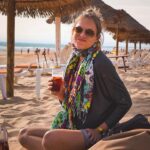 Ignacia Allamand Instagram – Había una vez un mundo, donde se podía viajar a lugares lejanos, y sentarse en la playa a tomar sangría viendo la puesta de sol sin mascarilla 🙃
Amo esta foto. El pelo chascón. El pañuelo de todos colores. La luz del crepúsculo y la cara de “Perdón por ser feliz con tan poco” 😂 que logró capturar una de mis mejores amigas de la vida. El vaso en la mano y la jarra que se asoma tímida por la esquina mostrando que gozar en grande nunca ha estado en discusión. El reloj swatch que ya en ese entonces estaba pasado de moda y el bolsito gris lleno de bolsillos y cierres, imprescindible para guardar mapas y guías turísticas y cuadernos y cámaras y puchos y encendedores. Ahora todo eso se condensa en un solo aparato y por suerte ya no fumo. 
¿Que nostalgia o no? No solamente de viajar, si no de viajar como antes. Sin WhatsApp, sin interrupciones, sin la necesidad de etiquetar ni de agregar la ubicación a nada. Entiendo la contradicción de hablar de esto precisamente en una red social, pero a veces me agarra el fantasma de los recuerdos y me remueve la guata y no me aguanto de compartir lo lindo que era la no necesidad de compartir 🤪 
Sobretodo los jueves, que gracias al #throwbackthursday tengo la excusa perfecta para contagiar mi saudade y mis recuerdos. 
Esto fue en Portugal. El año 2011. Tenía 29 años y quería comerme el mundo entero. O tomármelo para ser sincera. 
Durante esta pandemia he vuelto a mirar las fotos de ese viaje una y otra vez, compulsivamente, obsesivamente, como si verlas fuera una forma de viajar no solo a otros lugares, si no que también en el tiempo. Y a ratos eso me ha hecho muy, pero muy feliz. 
Otras me ha dado pena. 
Pero de esa linda, que más que tristeza, es emoción. 
¿Les gusta mirar fotos de otros tiempos?
¿Será que todo tiempo pasado fue mejor? 
Abrazo a todos.
Tomen agüita. 
Ánimo a los que lo están pasando mal. 
Besitos a los que tiran mala onda. 
Y besotes a los que mandan buena vibra. 
#queendelmuchotexto