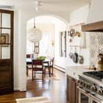 Lauren Liess Instagram – Another peek into that kitchen where you can spy the breakfast room through the archway. An antique family table became the centerpiece for the breakfast room which we decorated simply with antique Spanish colonial chairs and a hide rug for easy cleaning. A double pot rack over the old radiator is within reach of the new range. {tile is “sol di folium” from my collection with @architessa | cabinetry is the “bohemian” from my collection with @uniquekitchensandbaths and vintage runner   accessories are from @laurenliessandco | renovation by @carrmichaelconstruction | design by us at Lauren Liess Interiors | photo by @helennorman for my book #feelslikehome where I share all the “whys” behind the design of the entire house }