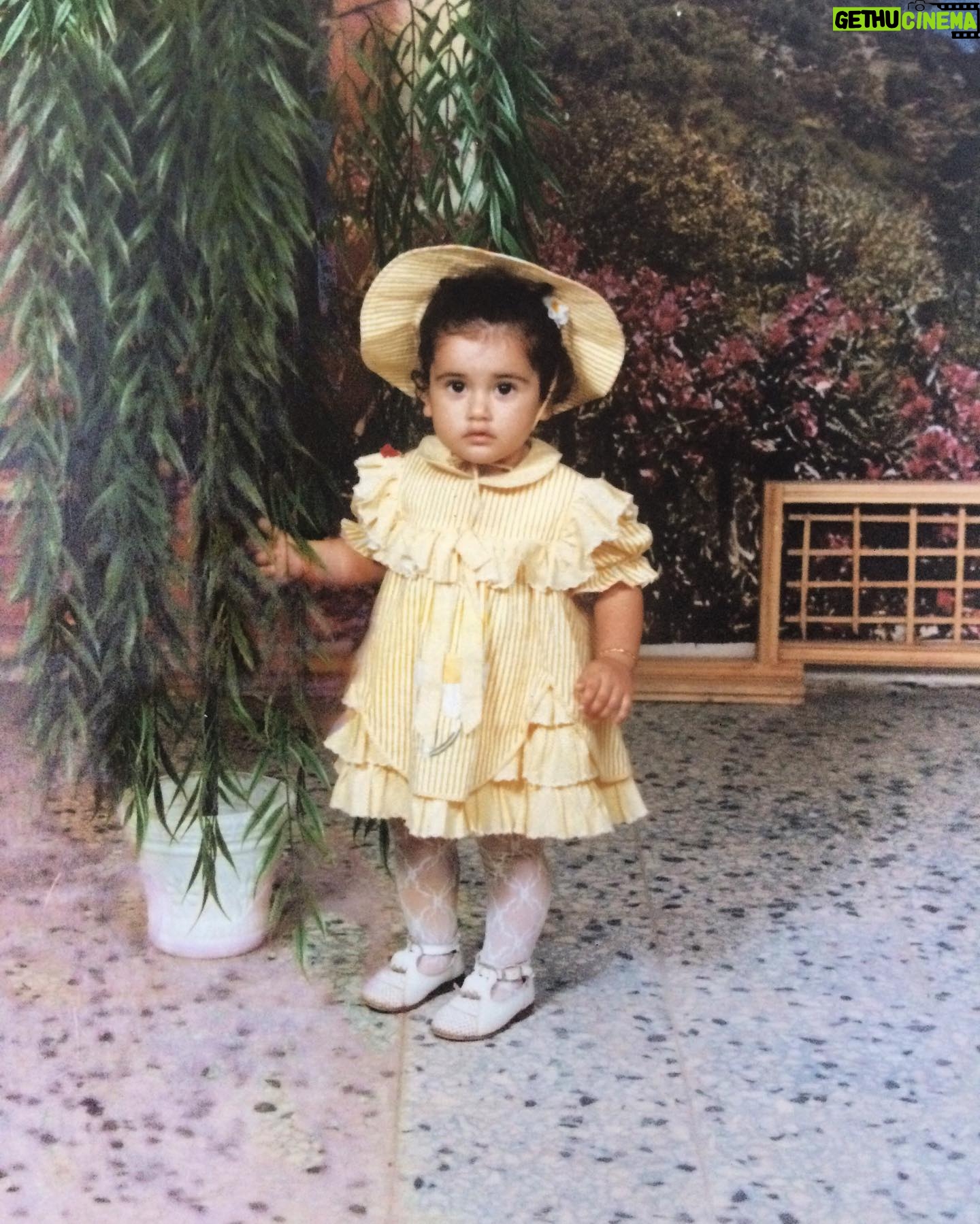 Neslihan Arslan Instagram - İlk (hatırladığım) fotoğrafçıda çekilen fotoğrafım bu.. Tam karşımda kimler vardı orası flu ama arkamda duran yalancı manzara görseli mesela dağına taşına kadar hâlâ aklımda.. Bilen bilir ki hâlâ da önümde, gözümün hizasında duranlardan daha iyi bilirim arkamda ne var ne yok.. Asla yerimde durmadığımdan, fotoğrafçı abimizi kısa süreliğine de olsa dinleyip poz vermem biraz gözleri yaşartmıştı diye de flu bi anı var yine kafamda bu arada.. Bir elbise giydirmişler, benden daha çok sevmişler o halimi, bilmediğim bir yere götürmüşler, tanımadığım bir abimiz çekildiğini hatırladığım ilk fotoğrafımı çekmiş, ben evin dışında kurallı ya da sistemli başka bi dünyayla ilk defa karşılaşmışım ki o’zaman da pek sevmemişim bu durumu falan filan… Neyse yani ez cümle; fikrim alınmadan kafam açılmaya başlamış.. Bir şeyle bazen çok ilgilenirken siz, başka çok şeyler de olabiliyor ilgilenilmesi gereken ve ıskalamak istemiyor olabiliyorsunuz onları da haliyle.. Çünkü bu bize farkında olmadan öğretilen ilk hayatta kalma bilgisi aslında; her şeyi görmen ve mümkünse değerlendirmen ya da zaten hiç elini bile sürmemen gerekir.’.. Sonra da klasik bi ‘rayına oturtma’ başlar yaş almayı anlamakla birlikte.. (Ya oturur ya da oturmaz, bu kısım başka..) Bazen bu fotoğraftaki gibi bi kal gelir/ gelebilir.. Onca şeyin ortasında aslında hafif ama onca şeyin ortasında olduğu için aslında ağır.. Fotoğraf çekildikten bir saniye sonra o yapraklarına dokunduğum çiçekle dans etmek istediğimden kendisini istem dışı yere devirmiştim.. Şu ara pek dans edesim yok ama yine de bi saksı devirirsem belki rahatlarım. İyi mi olur kötü mü olur bilmem bu arada.. Bu fotoğrafın sonrasının anısı iyiydi. Hadi başbaş..