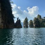 Rita Ferro Rodrigues Instagram - Dia 6 🤍 Como começar ? Antes de chegarmos ao lugar mais bonito que os meus olhos alguma vez vislumbraram fizemos uma viagem de duas horas de barco - porque este lugar situa-se no Parque Nacional Khao Sok , província de Surat Thani (Tailândia) e inclui os 165 km² do Lago Cheow Lan contido pela represa Ratchaprapha. Deve ser aqui que habitam todas as divindades da natureza - só pode ser aqui o seu refúgio - pois não é possível tanta beleza existir sem um qualquer toque divino. Aguardámos pelo barco com uma futebolada com crianças locais, fizemos a viagem com Sol, por entre várias tonalidades de água quente e doce que abraça escarpas magníficas e verdejantes, todas as cores da natureza em intensidade máxima, um espectáculo de poder do natural em bruto, uma parte do planeta muito preservada do toque humano. Chegámos ao @resort500rai com uma tempestade tropical a aproximar -se, bela e breve, e os pintainhos loucos de alegria, aos mergulhos à chuva , um descontrole de emoções ( tão bom !) perante o cenário de sonho. Totalmente sustentável , este resort constituído por pequenas , simples e confortáveis casinhas de madeira, munido de painéis solares, caiaques ( só saímos dos quartos nestes barcos que estão atracados à frente de cada habitação ) está totalmente integrado no parque natural. A partir das 22 h exige -se silêncio, o lema é “ disconnect to connect “ e por isso não há televisão e o serviço de wi - fi é muito limitado. A comida Thai é toda aqui confecionada - óptima - porque estamos no meio da selva, habitat de macacos, elefantes e outra bicharada fabulosa que vive em ambiente selvagem e que cumprimentaremos amanhã, numa das actividades que o resort proporciona. Não existe civilização por perto. Magia total ✨ Pintainhos e mãe vão dormir exaustos mas felizes. Amanhã é outro dia, cá estaremos para partilhar convosco. Muito amor aqui do Lago ❤️ #bestravel #bestravelviagens