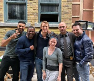 Sandra Mae Frank Instagram - Enjoying every moment with this badass cast on set of #TheSilentHour 😎🤘

#Thriller #Action #Film #Valletta #VallettaPictures #AGCStudio 

[image description]
A group of cast standing together in front of a building with bricks on set, all looking at the camera and smiling. (From left to right - Anthony, a light-skinned black man wearing a dark gray t-shirt with black jeans and has his peace hand up; Mekhi, a black man wearing a navy blue long sleeve with blue jeans; Joel, a white man wearing a black leather jacket and navy blue t-shirt underneath with blue jeans; Mark, a white man wearing a grey business outfit with a tie; Michael, a white man wearing a navy blue leather jacket with blue jeans; and Sandra Mae, white woman with blue/purple hair, braided in the front, wearing light gray long sleeve with grey sweatpants with black jeans underneath.

*FYI, @instagram - “Alt Text” is not DeafBlind friendly