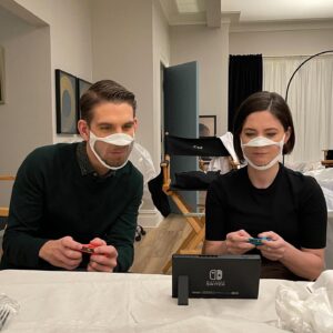 Sandra Mae Frank Instagram - We like to work hard…. and play hard! 🤓😎

#NewAmsterdam returns on February 22nd! 

#DamFam 💙

[image description]
Conner and Sandra wearing transparent masks in black tops, playing a game on Nintendo Switch in one of the NA sets, which looks like a living room.