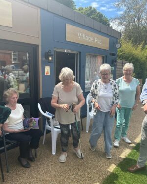 Anneka Rice Instagram - Oh my goodness. I went to Birkenhead, near Liverpool, today, to visit our Dementia Village, built on Challenge Anneka in 2022. It is flourishing. On a piece of wasteland a team of epic volunteers, builders, craftsmen, built an entire memory village - with pub, post office, record shop, cafe, bakers, cinema, bowling lawn, landscaped gardens! We worked in the pouring rain, in a recession, it was beyond stressful - but I thought my heart would burst, visiting it in the sunshine today, seeing what a difference it has made in this Wirral community. They now have over 400 volunteers helping out. The idea is that someone with dementia can wander safely round the village, dropping in on shops, listening to their favourite record, watching a film, having a singalong in the pub, doing whatever they want. It’s liberating for them and their loved ones because on every corner, sitting in the shops, offering them a cuppa in the cafe, there are carers to help them, chat to them, play bowls with them, sing with them. Each shop is curated to trigger memories. I went down a rabbit hole of memories seeing the Green Shield Stamps in the Post Office! IT IS BRILLIANT. I would love to see this rolled out across the UK. Well done @ageuk_wirral for having such vision 🩵🩵🩵 @age_uk #dementia @alzheimersresearchuk #village #ChallengeAnneka #charity #volunteers #community #joy @channel5_tv