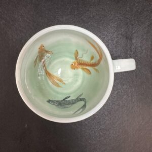 Emily Gravett Instagram - I really wasn’t sure how this would work. If the fish would be visible, whether the greens would shade down in the way I wanted, so I’m pretty delighted with how it turned out.  #ceramicsart #potterylove #porcelain #outofthekiln #teacupandsaucer