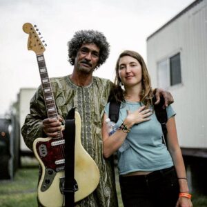 Emily Kokal Instagram - 6 years ago backstage at the Austin Psych Fest. 
Ibrahim from Tinarawin walked over while I was warming up outside the dressing rooms and motioned for the jag. I passed it to him - I don’t think we ever said words to each other - and he played around for a minute when Boris Allin came strolling up with this nice looking film camera and asked to take this pic. Love @tinariwen 
Grateful for this moment, and Boris for capturing it :)