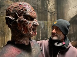 Greg Nicotero Instagram - One of the fun little Easter eggs that I “hid” in the episode of TWD I directed last weekend was a re-creation of the Freddy Krueger makeup from part one of “a nightmare elm street”. I always loved this character and all versions of the character i.e. David Miller and @yagherfx . this is a photo of my best bud and veteran of years of applying Robert’s make up @crognalegino touching up the likeness sculpted by @mikeyrots if you look closely you can see the striped sweater and a distressed glove #freddykrueger played by @garrettzehner