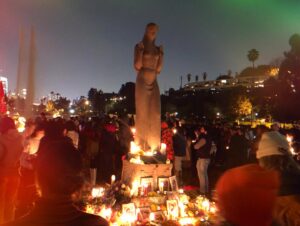 Julia Holter Instagram - from a @wawog_now event Jan 18: hundreds of Angelenos gathered for a vigil at Echo Park Lake to mourn and honor the lives of the writers, scholars, journalists, and poets among Gaza’s martyrs. This is an excerpt of Fariha Roisin reading “I Grant You Refuge” by Hiba Abu Nada (32, killed in her home in Khan Younis Oct 20 by Israeli airstrike)

Hiba Abu Nada (trans. Huda Fakhreddine)
1. I grant you refuge in invocation and prayer. I bless the neighborhood and the minaret to guard them from the rocket
from the moment it is a general’s command until it becomes a raid.
I grant you and the little ones refuge, the little ones who change the rocket’s course before it lands with their smiles.
2. I grant you and the little ones refuge, the little ones now asleep like chicks in a nest.
They don’t walk in their sleep toward dreams. They know death lurks outside the house.
Their mothers’ tears are now doves following them, trailing behind every coffin.
3. I grant the father refuge, the little ones’ father who holds the house upright when it tilts after the bombs. He implores the moment of death: “Have mercy. Spare me a little while. For their sake, I’ve learned to love my life. Grant them a death as beautiful as they are.”
4. I grant you refuge from hurt and death, refuge in the glory of our siege, here in the belly of the whale.
Our streets exalt God with every bomb. They pray for the mosques and the houses. And every time the bombing begins in the North, our supplications rise in the South.
5. I grant you refuge from hurt and suffering.
With words of sacred scripture I shield the oranges from the sting of phosphorous and the shades of cloud from the smog.
I grant you refuge in knowing that the dust will clear, and they who fell in love and died together will one day laugh.

A printed manifesto, collectively written by members of WAWOG’s Los Angeles chapter, was distributed to the crowd. Excerpts below:

WE ARE 100  DAYS IN AND STILL WE HAVE NOT ACHIEVED A CEASEFIRE.
JOURNALISTS, WRITERS, POETS, AND SCHOLARS ARE BEING TARGETED BECAUSE THEY ARE THE KEEPERS OF LIVING HISTORY.
WE DEMAND A PERMANENT CEASEFIRE, AN END TO ISRAEL’S SIEGE ON GAZA, AND AN END TO OCCUPATION NOW.