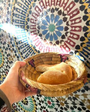 Maria Dias Instagram - O pão em Marrocos é um must-have em todas as mesas e tem variações dependendo da zona. Ele serve como faca para empurrar a comida para o garfo (ou para comer com as mãos) e é fofo o suficiente para absorver os molhos deliciosos das tajines e outros pratos suculentos.
O que vêem nas fotos chama-se khobs, deve ser um dos pães mais antigos do mundo, e leva farinha de trigo, sêmola de milho (às vezes), fermento e sal. No sul de Marrocos há um chamado Tafernout, de origem berbere e com um ar mais rústico e esburacado, e ainda exiete o Batbout, uns pequenos pãezinhos redondos feitos na chapa, tão fofos que ficam praticamente vazios no interior, ideais para serem recheados. 
A base dos pães geralmente é trigo, cereal base da alimentação marroquina desde há séculos - de onde vem o cuscuz também. Tradicionalmente é feito num Tanour, um forno de argila. No deserto é feito debaixo da areia quente. 
Nos restaurantes servem pão com tudo e de facto fica bem com tudo ☺️
