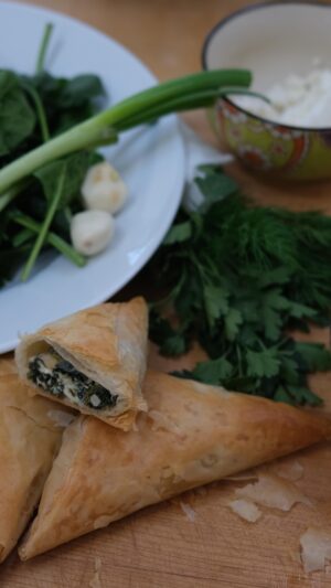 Michael Symon Instagram - This Sunday is Greek Easter so I’m bringing back my mom’s spanakopita recipe. A classic that is always a welcome sight on any table. 🥬🇬🇷 Enjoy!! 

You know what is also on Sunday? The risk taking and simplicity challenge on 24 in 24. If you haven’t caught up on all the episodes they’re available now! 
#24in24 Last Chef Standing 
Sundays 8|7c > @foodnetwork @streamonmax 

Spanakopita 

Yield: 15 pieces
 
Ingredients
¼ c olive oil
1# fresh spinach leaves
½ tbl kosher salt
 
½ c thinly sliced green onion
2 cloves minced garlic
¼ c  finely chopped parsley
¼ c finely chopped dill
3 c crumbled Greek feta
4 whole eggs, beaten
½ c of pine nuts (optional)
2 tbl olive oil
1 tsp kosher salt
Pinch of freshly grated nutmeg
 
1 pound #2 phyllo sheets
1 c unsalted butter, melted
 
Directions
Sweat the spinach in 2 tbl of olive oil until softened and wilted. Season with pinch of salt.
Pour into a strainer and allow to strain for 30-90 minutes. 
Place into a tea towel and wring as much excess moisture as possible. (Yield: ¾ # of pressed spinach.) Roughly chop and add to a mixing bowl.
Add all remaining ingredients to the spinach except the phyllo and butter and mix to combine.
Lay out 1 sheet of phyllo and brush with melted butter. Place another layer of phyllo on top and brush with butter. Fold in half lengthwise and brush with butter.
Place ½ c  of spinach filling on the phyllo, closest to you.
Begin folding like a football, brushing butter in between each fold.
Place seam side down on a parchment lined sheet tray and bake at 350* for 15 minutes, until golden brown and crisp. Enjoy.