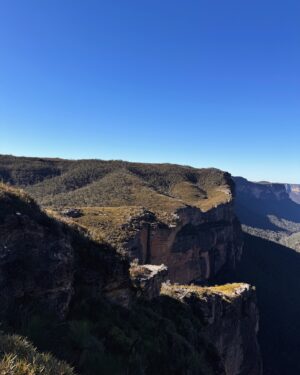 Rae Johnston Instagram - The sun and moon sharing the sky, sandstone paths, grass trees, huge ancient cliff faces, and that beautiful river flowing in the deep valley below 🤎 

Today’s walk on Wiradjuri, Darug & Gundungurra Country - making the most of the clear skies while they last, looking wet and below freezing next week! 

#bluemountains #rigbyhill #piercespass #wiradjuricountry #darugcountry #gundungurracountry