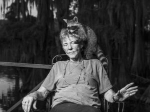 Robin de Puy Instagram - New episode! #linkinbio 

Caddo Lake is as smooth as a mirror’s surface and filled with large yellow flowers proudly reaching for the sun. “When the flower has finished blooming, the fruit remains, '' says Chaz (38), born and raised in Uncertain, a small village bordering the lake. He picks up a ripe piece of fruit: “Here, have you ever tasted this?” Without hesitation, I bite into the sweet seeds of the American lotus. 

Uncertain is on the border of Texas and Louisiana. It has 85 inhabitants and is buried deep in swampland. Large moss-covered cypress trees give the village a somewhat ghostly appearance. The town is perfect for anyone who does not want to be found. People take care of their own business here and help from outsiders is not welcomed. 

“The lake raised me. I am a real swamp-rat.” Chaz's beard blows gently in the wind. “We have everything we need here: water, food, and medicine. Life doesn't come from a store. It starts in nature.” It sounds like paradise, and I would rather not leave.

When I ask Chaz who I should definitely meet here, he immediately replies, “Dottie! She used to be my teacher and she's the SuperWoman from Uncertain.”

Before long, I found her. Dottie is 83 years old and still likes to ride her Harley Davidson, sometimes with a cape - she is SuperWoman, after all. She clearly loves life as well as her raccoon, Willow, who is always perched on her neck or in her lap. 

Dottie owns a lot of land, including a small graveyard. “Always wanted one.” It came in handy when her husband Billy passed away last year. Wrapped up with cloth, he was six feet under within twelve hours. He thought he was dying of an infection because he had given a baby raccoon mouth-to-mouth, but Dottie disagrees. 

“The average age of an Uncertainer is only 58. Fresh vegetables are hard to find here. And almost all of the food is deep-fried. Combined with frequent use of alcohol and cigarettes, it doesn't appear to be the best way to grow old. And then there's something about mercury in the water.”

Mouths full of American lotus seeds and acclaimed scenery, yet it’s less like paradise after all. As it turns out: nothing is certain in Uncertain.