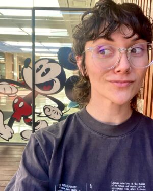 Alyson Stoner Instagram - Can we believe the first season of Phineas and Ferb premiered on this day 16 years ago? 😱

Well, we’re back at it again. Stay tuned 👀

Alt text: The first slide is a selfie of Alyson wearing glasses and a grey shirt, standing in front of a Mickey Mouse decal. The second slide is a video of younger Alyson in a red shirt in a studio setting talking about their character, Isabella. The third slide is a video selfie of present day Alyson in a grey shirt within a recording studio. The final slide is a video of younger Alyson, singing in a studio while wearing a tan jacket.