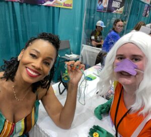 Anika Noni Rose Instagram - A wonderful day at @galaxyconraleigh! Thank you kind, beautiful people for all of the gifts you gave and the gifts you shared-sometimes all in one. 

Thank you to all of you who wore masks.

Thank you to every one of you who stopped by and shared your loving hearts with me. 

See you tomorrow!

Remember, if you have a mask, if you just want any to be cautious, if you THINK you don’t feel well, please mask up. If you KNOW you’re sick, consider staying home. These lungs can’t take a bout with the 🦠

Let’s keep each other safe out here! 
See you tomorrow for the panel!
💚👸🏽

1. @Raycayz, I got my sticker and I love it! Thank you!!
💚
2. Coloring from sweet baby Mila, and first friendship bracelet of the weekend 
💚
3. Gorgeous embroidery frog necklace from @natsnostalgicstitches
💚
4. Amazing Tiana art by @flocolores
💚
5. Some more gorgeous art, by sweet @artbyannae . Thank you for your beautiful talent and huge heart🥰

Thank all of you for a beautiful day!

Hair I love by @indiamhammond 
Onesie by @martinesdream 

#galaxyconraleigh #galxycon #princessTiana