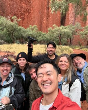 Benjamin Law Instagram - 24 HOURS IN ULUṞU

Shot this lil’ segment in beautiful Aṉangu Country after a rare evening of rain. It meant we could see the true black shade of the monolith under its red rust foundation, and how freshwater gathers at the base of the structure – which is taller than the Eiffel Tower, more ancient than the first dinosaurs and runs another 2.5km underneath.

Thanks to Uncle Sammy Wilson – son of Paddy Uluṟu! – for welcoming and handpicking bush tomatoes for us (an unexpectedly perfect mix of tomato and banana), and this dream team crew of the two Dans, Pariss, Bruno, Sarah and Toby. 

And, of course, icon Julia Zemiro who can do no wrong and for whom I would walk directly into peak hour traffic with my eyes closed if she asked. 

On yr TVs soon. Palya, peeps. ✌🏿✌️✌🏼