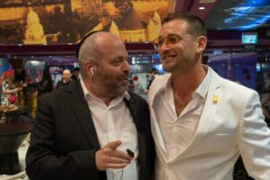 Dean Miroshnikov Instagram - רק לפני ארבעה חודשים יצאתי מעזה והייתי באימון גדודי, שנייה לפני שאנחנו נכנסים לרפיח. במקביל, בין יציאות, אני מנסה לתאם את התאריכים לטיסה לגאורגיה עם כל צוות הצילום של “גרובייס הפקות”. לאחר ימים של תיאומים, אני נאלץ להודיע ליהודה: “סליחה, אחי, אבל אין סיכוי שאני יוצא עכשיו לצילומים. אנחנו במלחמה.” לא יתאפשר.

כמה דקות לאחר מכן, אחד הקצינים בפלוגה שואל אותי: “מה אתה מבואס פולצ׳ק?” אני מספר לו שהרגע וויתרתי על תפקיד. הוא שאל אותי ״באיזה סרט מדובר?״ סרט אקשן של במאי חרדי, יהודה גרובייס. “נקמה יהודית 6״. בטח אתה לא מכיר.
הוא נתן לי חיוך מאוזן לאוזן..
“יהודה גרובייס? אני גדלתי עליו.” שנייה אחרי זה הוא הוציא את הכיפה ממכנסי הב׳... “אין סיכוי שאתה מוותר על התפקיד. דבר עם המפקד שלך״.
ארבעה חודשים אחרי, אני כאן, בסינמה סיטי ירושלים. אולם מפוצץ (400 איש) ואין מקום פנוי לשבת. אשתי המהממת כאן לידי, ואני בהודיה.
המקום היחיד עד אתמול.. שבו האמנתי שיש “אחדות״, אמיתית, היה הצבא. מקום שבו אין דעה פוליטית, ולא משנה אם אתה חילוני, חרדי, מוסלמי, נוצרי, הומו, דרוזי, אוקראיני, מרוקאי, אתאיסט או כל דבר שתבחר. צה”ל היה המקום היחידי שבו הייתה לי האמונה שה״ביחד״ עובד על אמת. כי יש מטרה ברורה. לתת בטחון למדינת ישראל.
אתמול.. נפתחה בליבי עוד דלת של אחדות – הקולנוע. בחיים לא האמנתי לפני ארבעה חודשים שנעמוד כאן, בסינמה סיטי ירושלים, המקום המסחרי והחילוני ביותר בעיר הקדושה בעולם, ובו נקרין את סרטו ה-109 של יהודה גרובייס – “נקמה יהודית 6”. והיד עוד נטויה. גם החרדים וגם החילוניים יכולים ליהנות מאותה היצירה. מאותו סיפור. 

תודה לך, יהודה, שנתת לי הזדמנות להיות ברגע היסטורי זה של הקולנוע הישראלי, שבו סרט של במאי חרדי מגיע לקולנוע מסחרי. אני גאה לעמוד כאן, לצד כל יוצרי הסרט.

את התפקיד “אלי”, אני מקדיש למפקד שלי מהשירות בשייטת 13 – אלי גינזברג. אלי היה גיבור גדול. הוא נהרג בקרב לבלימת הטבח בבארי ב-8.10. אלי השאיר אחריו את מלכי אלמנתו וארבעה ילדים. יהי זכרו ברוך. אלי היה גיבור, וככה אני רוצה שיזכרו אותו.

זאת הזדמנות חשובה לזכור שיש לנו עוד 115 חטופים בעזה, שחייבים לחזור הביתה עכשיו. רק ביחד ננצח בכל דבר.

מהיום הסרט מוקרן ברשת סינמה סיטי בבתי קולנוע מובחרים.
על הצילום: בוריס קאזדן, אור בן אסולין
על החליפה @names_il 
על השמלה @drorkontento 
עיצוב שיער @amirbakshihair