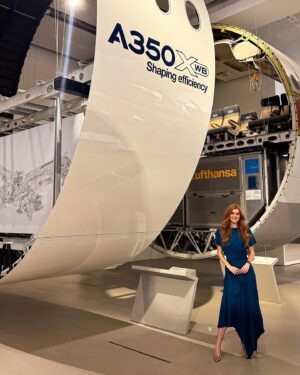 Jessica Gagen Instagram - An A350 fuselage! ✈️😎

The science behind a fuselage is amazing; torsion, bending, shear, compression and tension are all factored into its design… But what’s taking up more headspace at the moment is trying to figure out how they got this whopper in here 🤣

My blue dress is by @kevanjonfashion 👗

#STEM #aerospace #engineering #a350 #airbus #munich #aviation #engineer #science #technology #maths #girlsinSTEM