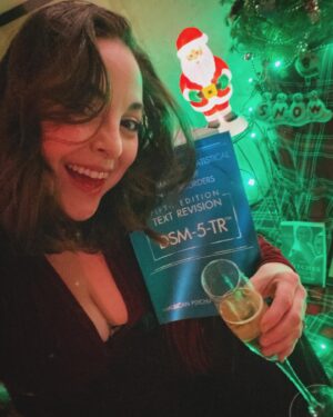 Brittany Curran Instagram - The amount of selfies I just took with my very own DSM-5-TR could be studied as a pathology in it of itself… Anyways, @jamesisntcool got me the BEST CHRISTMAS PRESENT! Literally cried happy tears when I opened it 🫶🏻🎄♥️💚🧠📚 

#merrychristmas #christmaspresents #dsm5tr