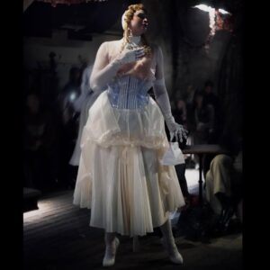Gwendoline Christie Instagram - Maison Margiela Artisanal 2024 Collection by @jgalliano .

Look 44
Overdress and an underdress in white silk taffeta with retrograding in seeping silicone coating worn over a blue-and-white striped cotton poplin stripe-tease corset and a white silk knitted bodysuit, underpinned by a silicone hip prothèse matching the skin tone of the  muse. A porcelain-imitation moulded leather breastplate, a white leather small top-handle Snatched bag, white silk stockings, and white leather pumps by Christian Louboutin for Maison Margiela enveloped in white stocking material. White paper maché, clay, string and stretch-tulle lay doll gloves overlaid in white silk jersey.
Model @gwendolineuniverse

@maisonmargiela 🤍