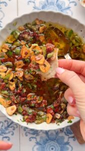 Laura Vitale Instagram - Meet your new favorite bread dip yall, this sun dried tomato version is literally INSANE!! With all the fresh bread I bake on the daily I need a little something for dipping ya know?!! Recipe below, do give it a whirl! 

Recipe:
1 cup of olive oil (no need for really strong extra version) 
4 cloves of garlic thinly sliced 
Pinch of hot pepper flakes 
1/3 cup finely chopped sun dried tomatoes packed in oil
1/3 cup finely chopped castalvetrano olives
2Tbsp chopped basil
2 tbsp chopped parsley 
1/4 cup grated parm
1 tsp Italian seasoning
Pinch of salt 
1 tbsp of good balsamic vinegar 
 
Once the the garlic becomes golden brown, remove to cool slightly. Then mix all together when the garlic oil is still warm to really bloom those flavors. Allow to cool completely before serving.